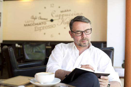 Portrait of businessman sitting in a coffee shop with notebook writing down something