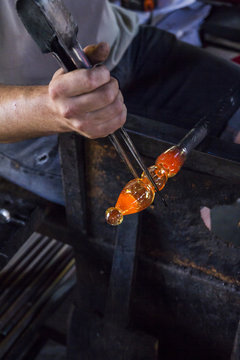 Man working with molten glass using a tweezers in a glass factory