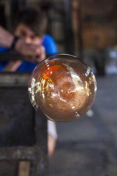 Man blowing molten glass with a tube in a factory