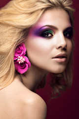 Beautiful young blonde woman with creative make-up color and flowers on the ears. Beauty face. Art makeup.