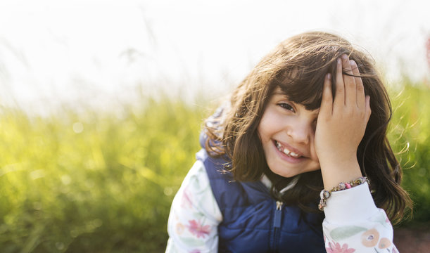Portrait of smiling little girl covering eye with her hand