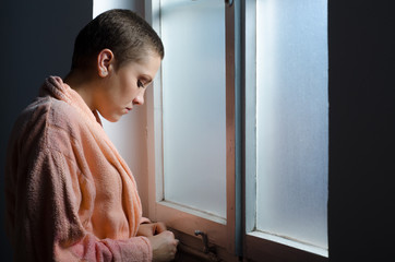 Young cancer patient standing in front of hospital window