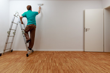 Mann auf Leiter beim Streichen der Wand
