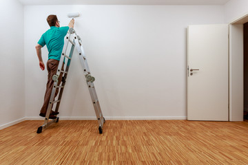 Mann auf Leiter beim Streichen der Wand