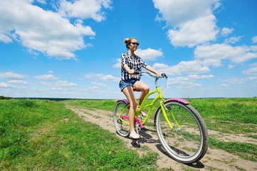 Fototapeta premium Beautiful girl riding bicycle outdoors across the green sunny field