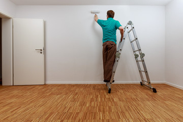 Mann auf Leiter beim Streichen der Wand