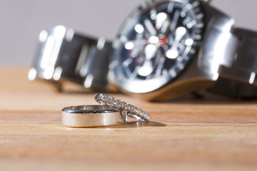 A man's and woman's wedding rings on a bedside table. A man's wrist watch is in the background out of focus.