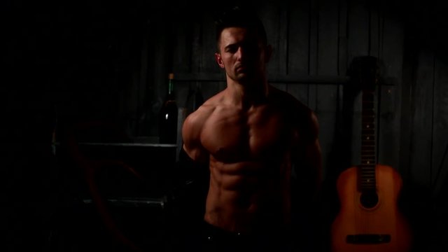 Attractive young man taking shirt off, undressing to reveal lean, muscular torso in studio shoot on black background 