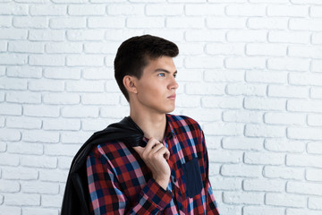 Handsome young man in casual clothes, standing against white brick wall