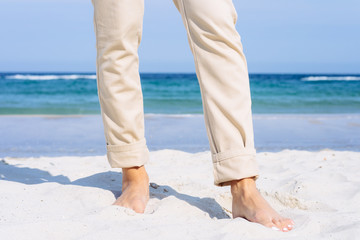 Close-up of female legs in beige pants barefoot on the beach