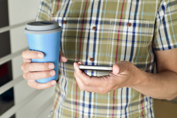 man with a cup of coffee or tea using a smartphone