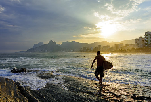 Surfer walking over rocks preparing to enterin the water during sunset on Ipanema beach, Rio de Janeiro