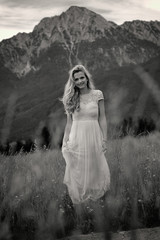 Fototapeta na wymiar Junge Frau steht in einem langen Kleid auf einer Wiese vor dem Hochstaufen