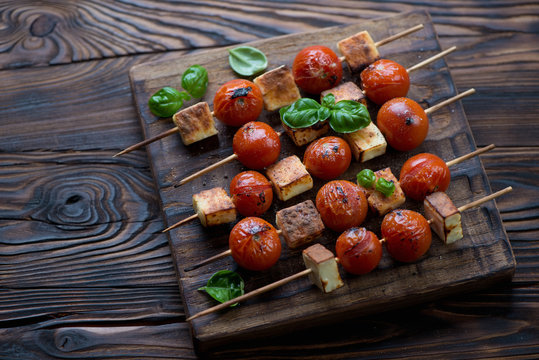 Rustic wooden serving board with tomatoes and cheese skewers