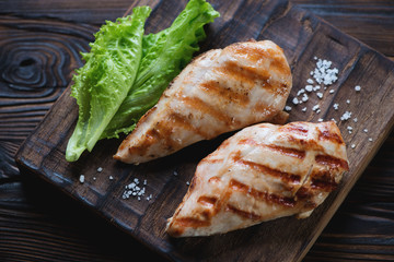 Closeup of two grilled chicken breasts on a rustic serving board