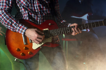 Obraz premium Young man playing electric guitar on lighted foggy background