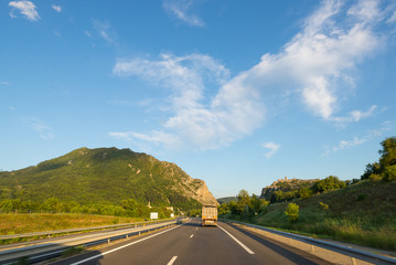 Paved two lane road crossing mountains and forest in scenic alpine landscape and moody sky. Panoramic view from car mounted camera. Summer adventure and roadtrip in the Italian French Alps.
