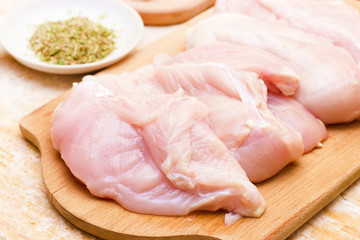 Close-up of chicken on wooden board on the kitchen table. In the background is plate with spices and chopped onion