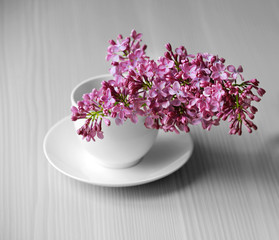 Purple lilac flowers in a cup on white wooden table background
