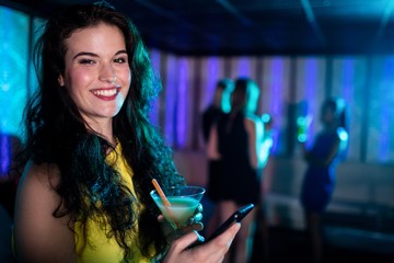 Beautiful woman using mobile phone while having cocktail