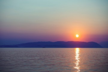 Sunset falling behind mountains is viewed from a beach on greek island
