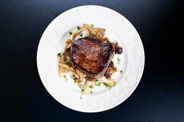 Tasty Beef Mignon steak with mushrooms and herbs on plate.