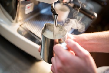 Fototapeta na wymiar Waiter steaming milk at the coffee machine