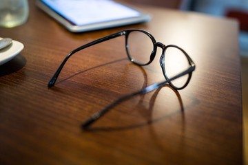 Close-up of spectacle and mobile phone on wooden table