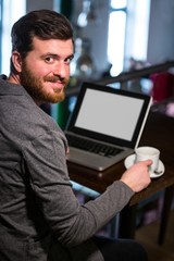 Man holding coffee cup and using laptop