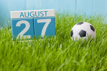 August 27th. Image of august 27 wooden color calendar on green grass lawn background with soccer ball. Summer day. Empty space for text