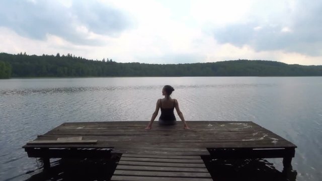 Young woman sits on a wooden pier on the lake, rear view