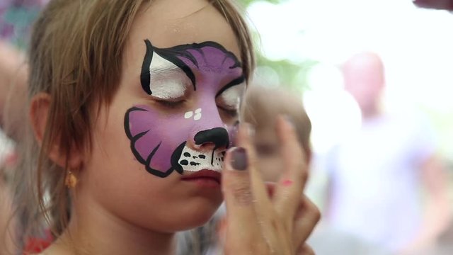 The artist paints face painting on the face of the girl
