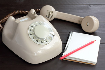 old connections of communications and technology / old phone with a notebook and red pencil on a dark wooden background 