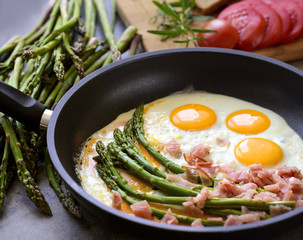 Fried eggs with asparagus, ham and egg shell on a dark stone board