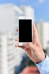 Closeup on hand holding mobile cell phone over city buildings business background.