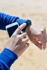 Person holding mobile phone checking connection using watch. Sunny background
