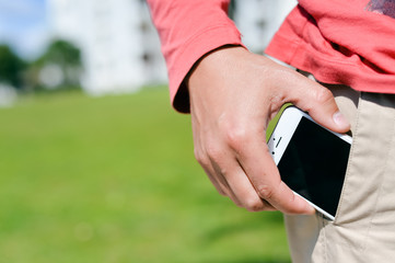 Closeup man taking smartphone from pocket on sunny outdoors background