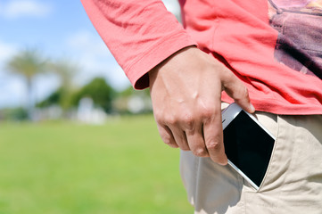 Closeup man taking smartphone from pocket on sunny outdoors background