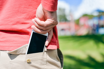 Closeup man taking smartphone from back pocket on sunny outdoors background