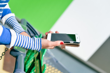 Female holding mobile smart phone in hand and shopping cart in store