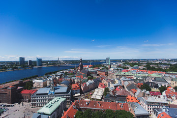 Obraz premium Beautiful super wide-angle panoramic aerial view of Riga, Latvia with harbor and skyline with scenery beyond the city, seen from the St. Peters Church observation tower, sunny summer day