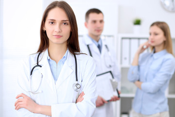 Fototapeta premium Young beautiful female doctor smiling on the background with patient and his doctor in hospital. High level and quality medical service concept.