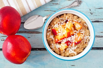 Bowl of overnight breakfast oats with diced peach and coconut, overhead scene on rustic blue wood