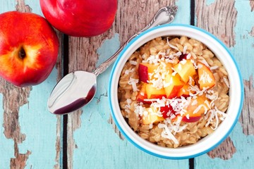 Bowl of overnight breakfast oats with diced peach and coconut, overhead scene on rustic wood