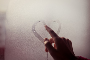 Person drawing heart on wet window with finger
