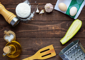 The ingredients and tools for cooking pancakes from zucchini  on a dark wooden background. top view. In the middle of the free space for text
