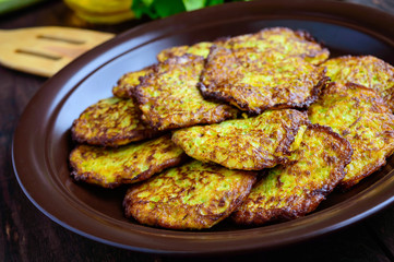 Golden pancakes from zucchini on a clay plate on a dark wooden background. Close-up.