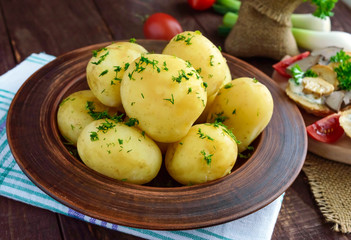Young boiled potatoes with butter and dill in a clay bowl on a wooden background