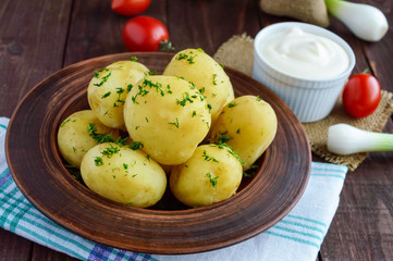 Young boiled potatoes with butter and dill in a clay bowl on a wooden background. Close up