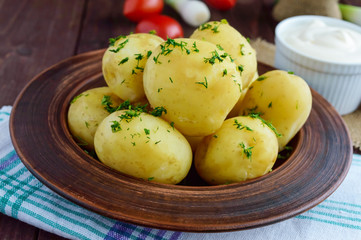 Young boiled potatoes with butter and dill in a clay bowl on a wooden background. Close up